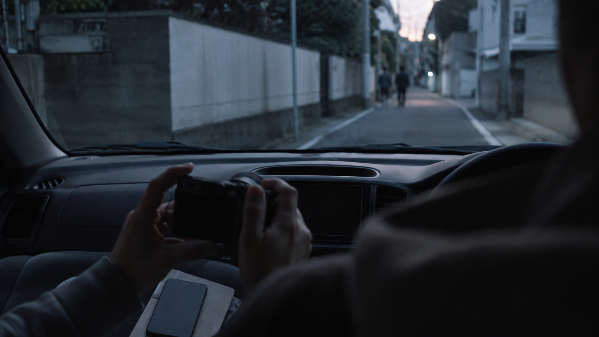 夜の住宅街で車の中から様子をうかがう人物の後ろ姿